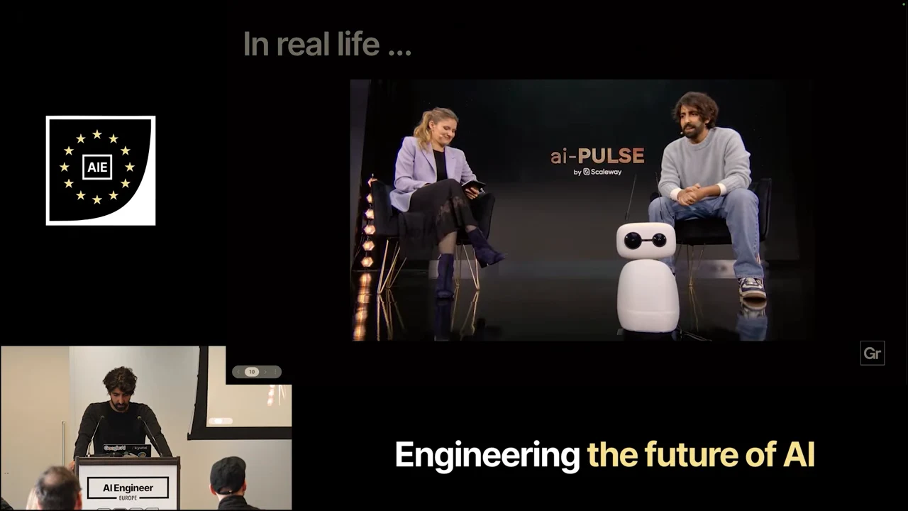Embedded video showing two seated people with a small white robot between them on an ai-PULSE stage.