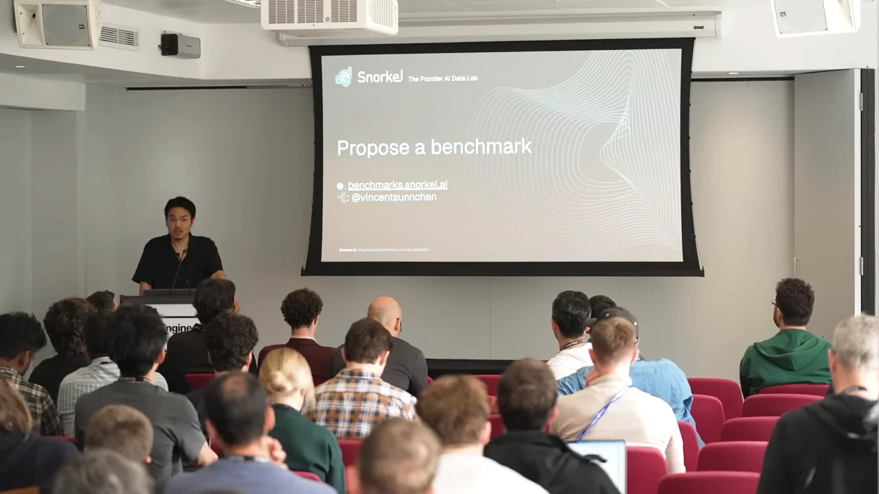 Presenter beside a projected Snorkel slide titled “Propose a benchmark,” with a website link and social handle below.
