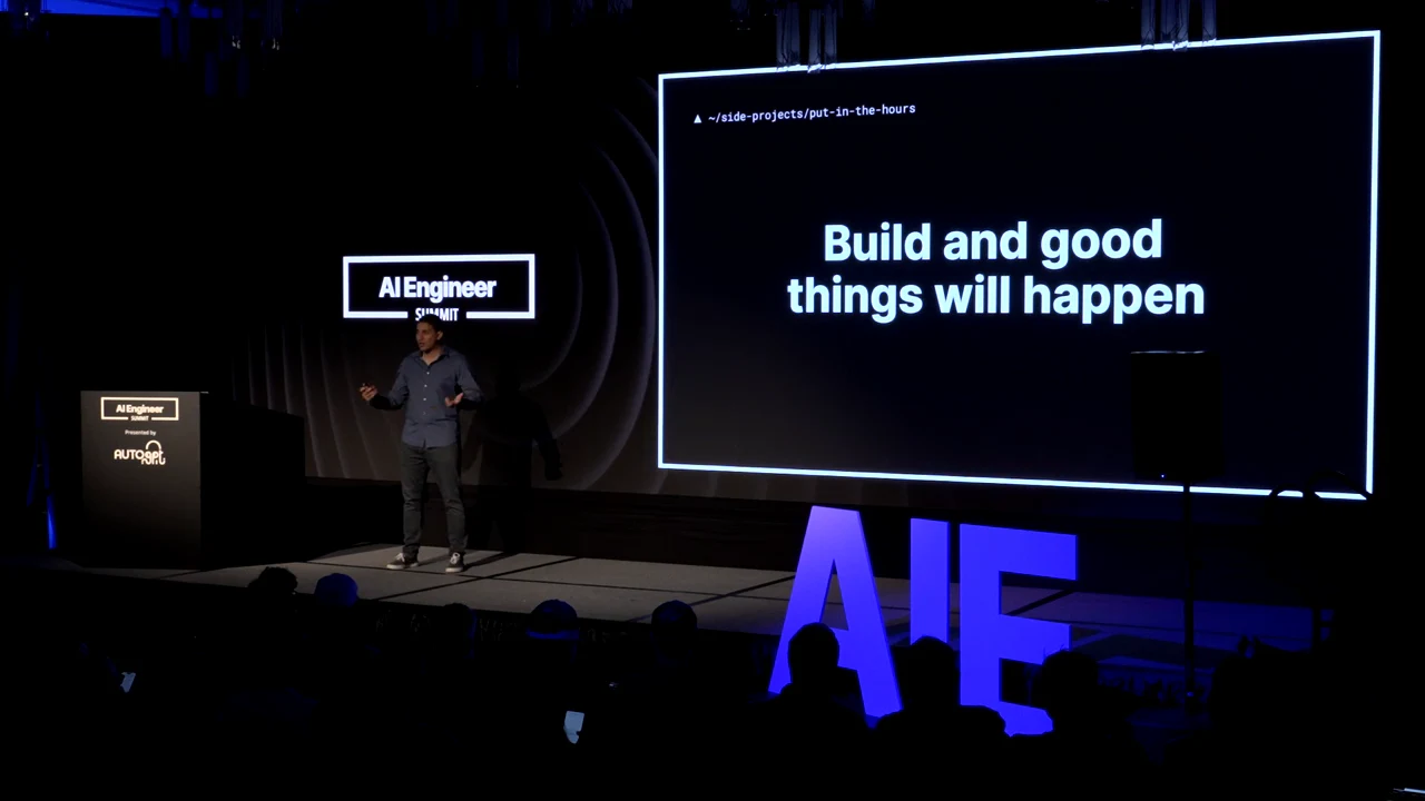 Wide stage view with the speaker beside a slide reading “Build and good things will happen.”