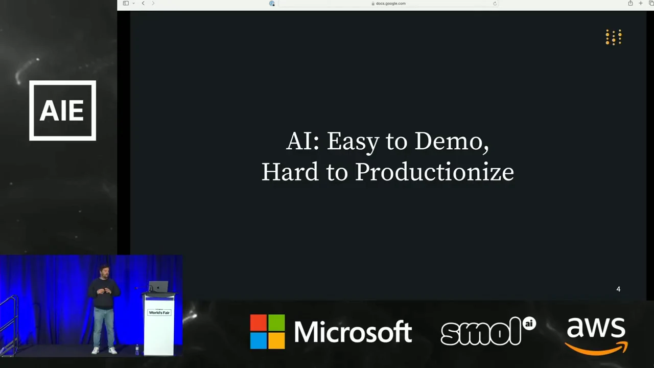 Dark slide displaying “AI: Easy to Demo, Hard to Productionize,” with the speaker inset at lower left.