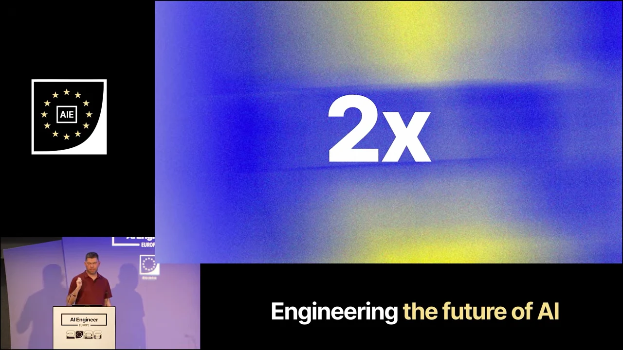 Large white “2x” centered on a blue and yellow background, with the speaker inset below.