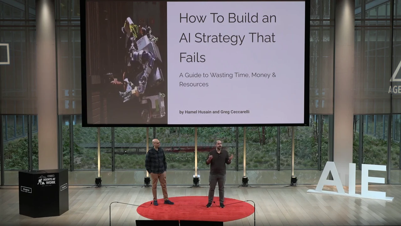 Two presenters stand beneath the talk’s title slide, which pairs the title and subtitle with a robot image.