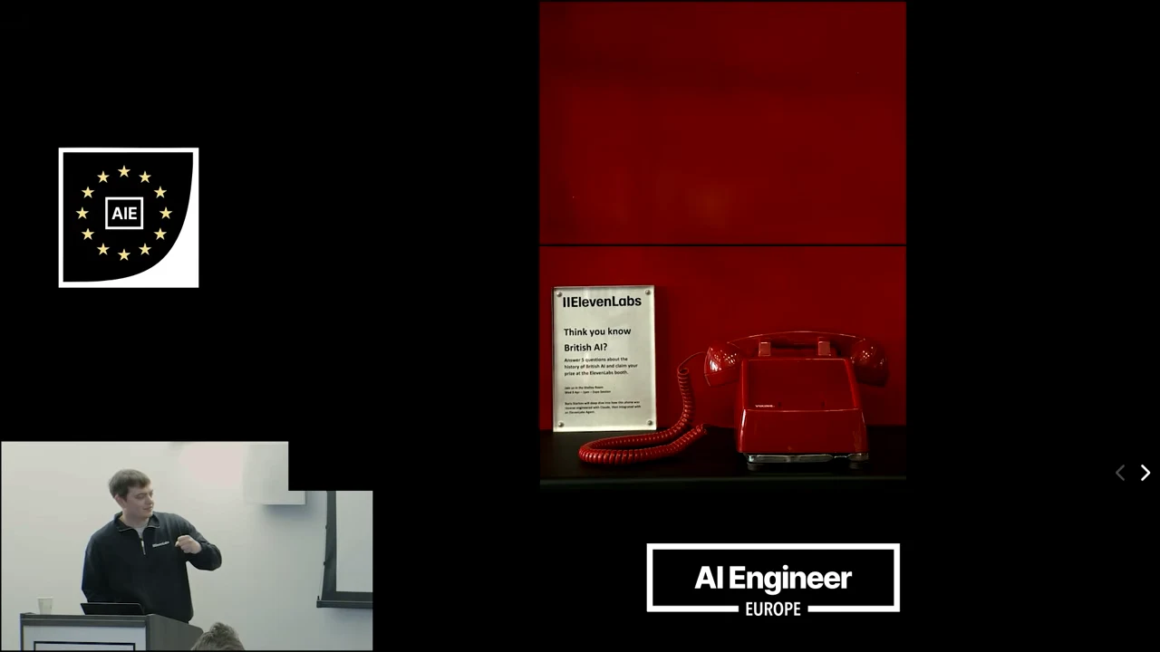 A red corded telephone beside an ElevenLabs sign in a red booth, with the presenter inset at lower left.