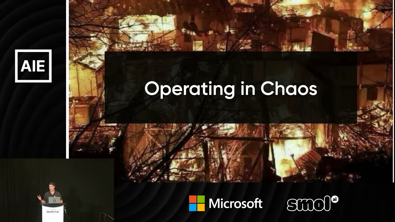 A burning building behind a dark panel reading “Operating in Chaos,” with the speaker visible in a small inset.