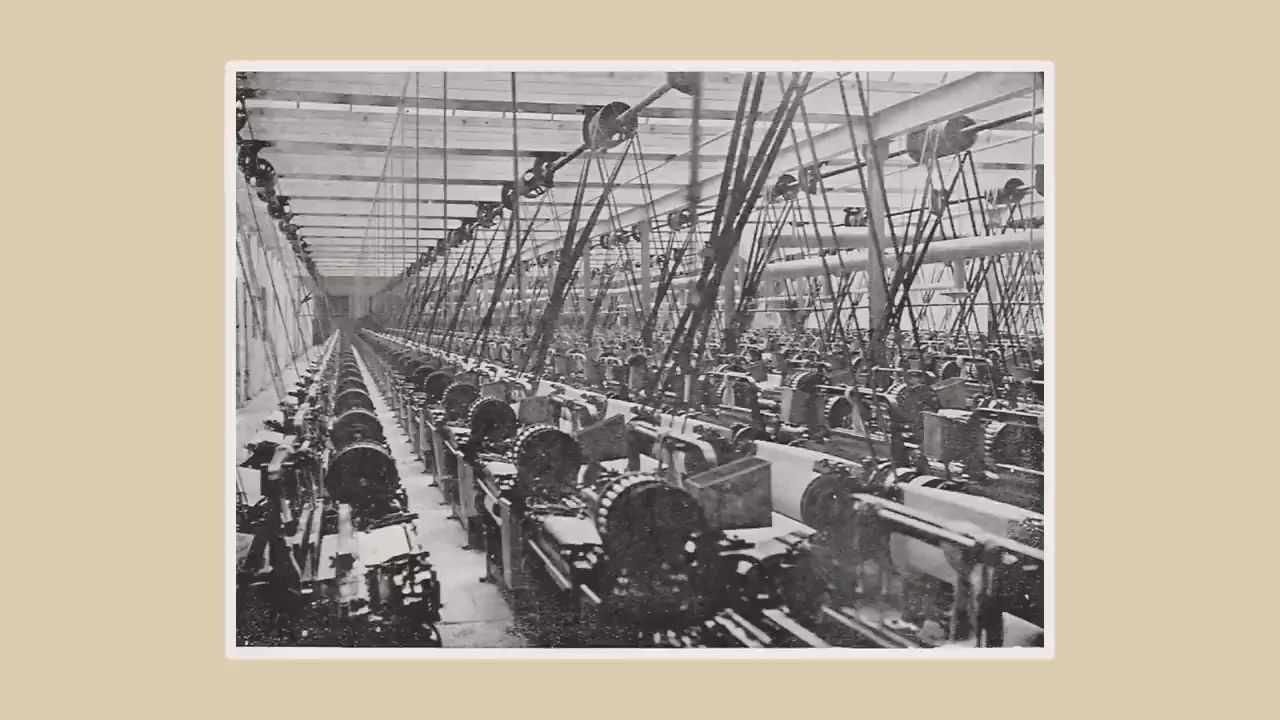 Black-and-white photograph of rows of factory machines beneath a dense network of overhead belts and shafts.