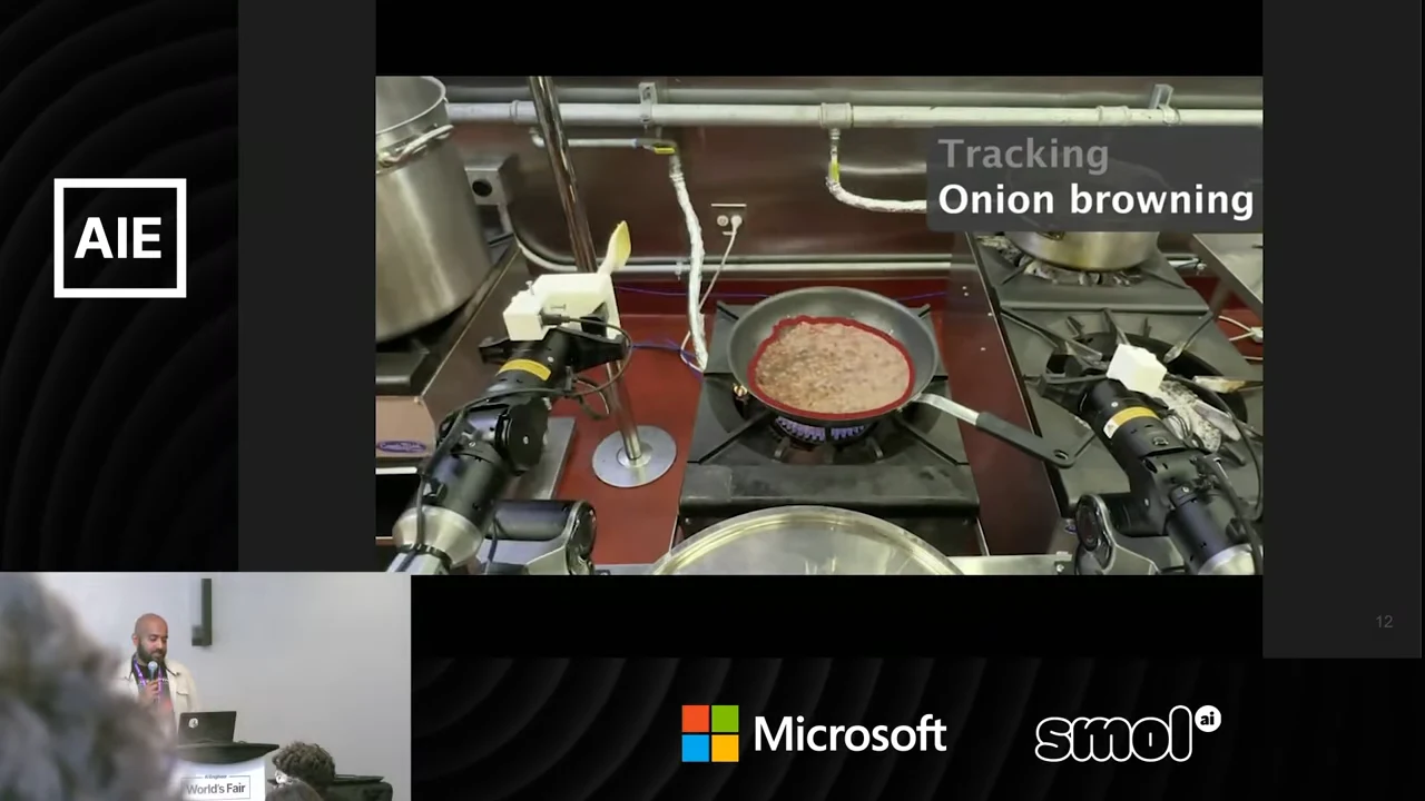 Robot arms surround a pan on a stove, with a red outline around its contents and the overlay “Tracking Onion browning.”